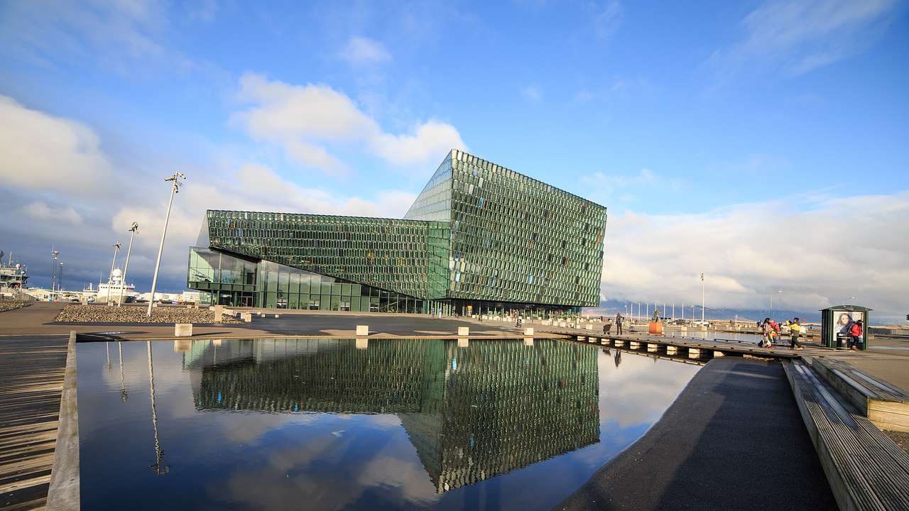 A structure made of glass panels next to a pond on a partly cloudy day