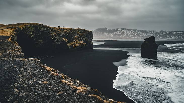 A black sand beach with white sea waves breaking on the shore beside mountains