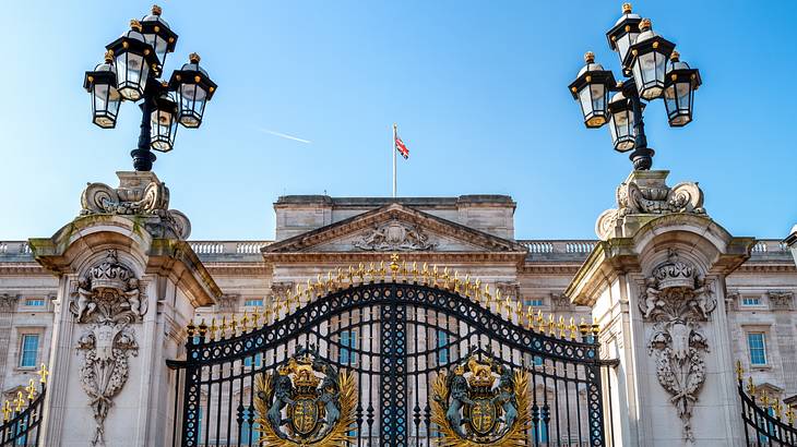 A steel gate with two posts adorned by regal details in front of a palace