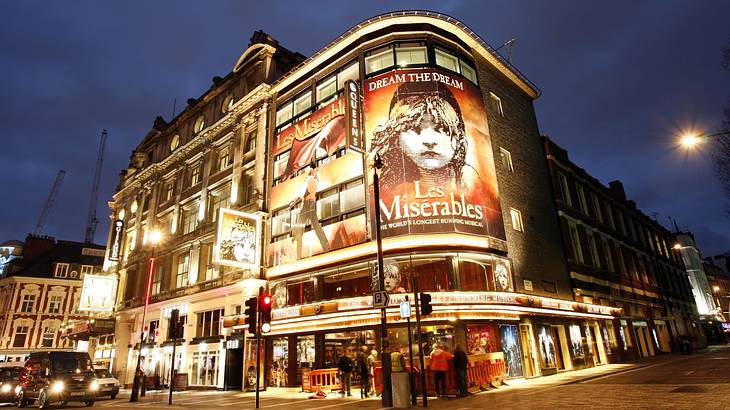 A theater with large posters of a show illuminated by lights under the dark night sky