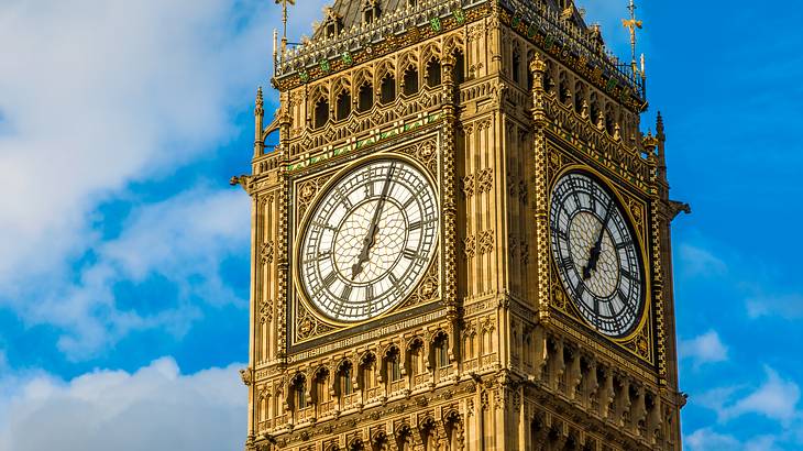 A clock with black numerals within a golden tower against a partly cloudy blue sky