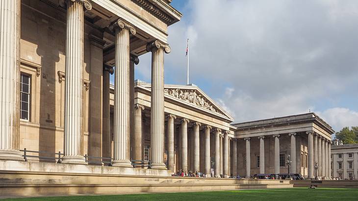 A large stone building with columns next to a green lawn under a cloudy sky