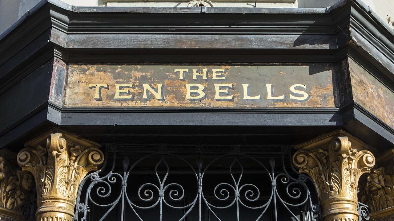 A building entrance with two golden posts, steel bars, and a "The Ten Bells" sign