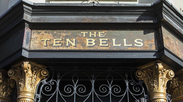 A building entrance with two golden posts, steel bars, and a "The Ten Bells" sign