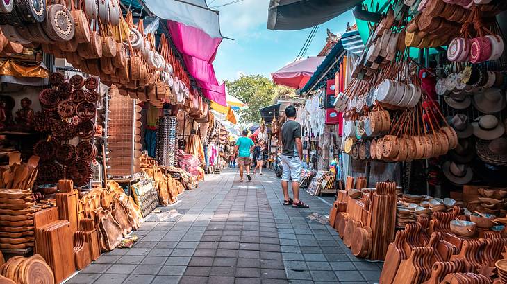 A path with market stalls on each side selling bags and wooden boards