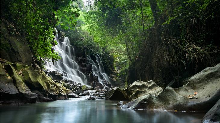 A small waterfall running over rocks next to a pool and greenery