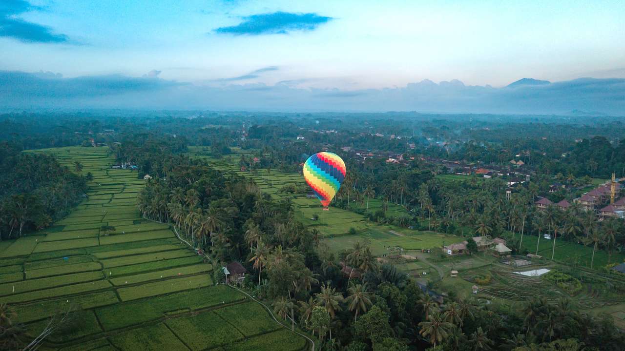 A hot air balloon flying over green fields and trees at sunrise