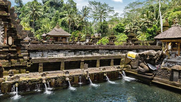 A pool surrounded by stone structures and green trees