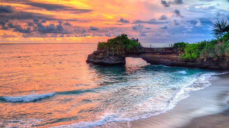 Natural rocks with trees on them next to the ocean at sunset