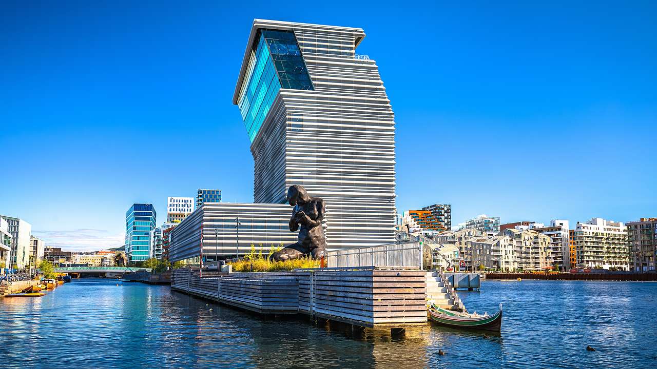 A modern building with a sheet-like design near a sculpture and a body of water