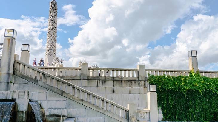 Concrete stairs leading to an elevated area with people near a tall sculpted monolith