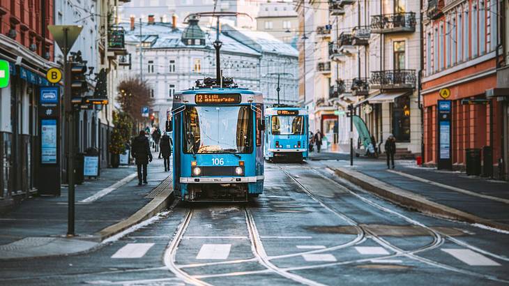 A tram near buildings and the pavement with people walking on it