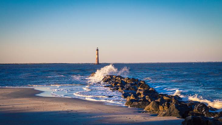 A lighthouse on the background of waves crashing into a rocky breakwater by the shore