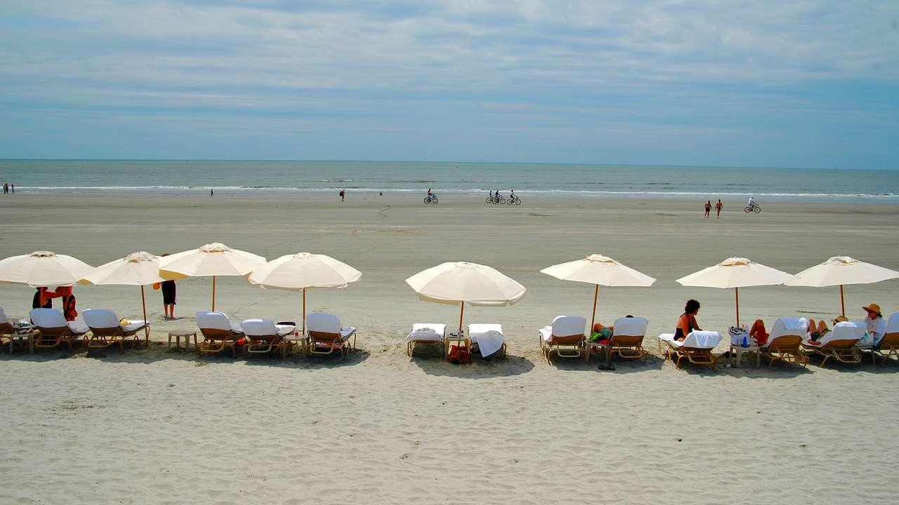 People relaxing on beach chairs with white umbrellas and biking along the shore