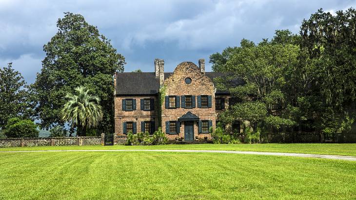 A grassy lawn in front of an old brick house surrounded by trees