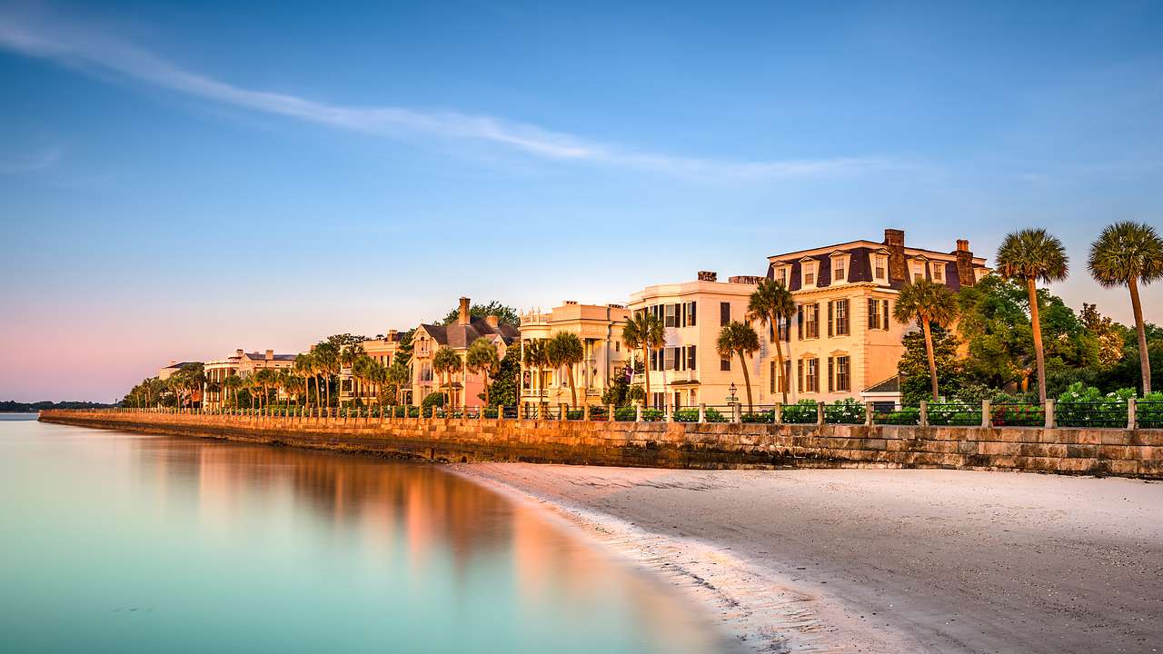 A row of antebellum mansions and palmetto trees by a beach against a colorful sky