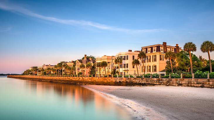 A row of antebellum mansions and palmetto trees by a beach against a colorful sky