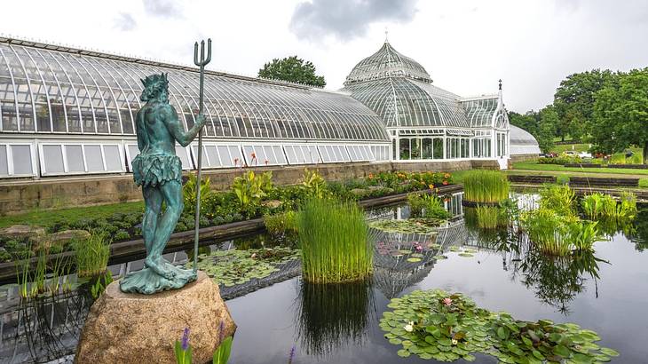 A green statue in a pond with a glass conservatory to the side