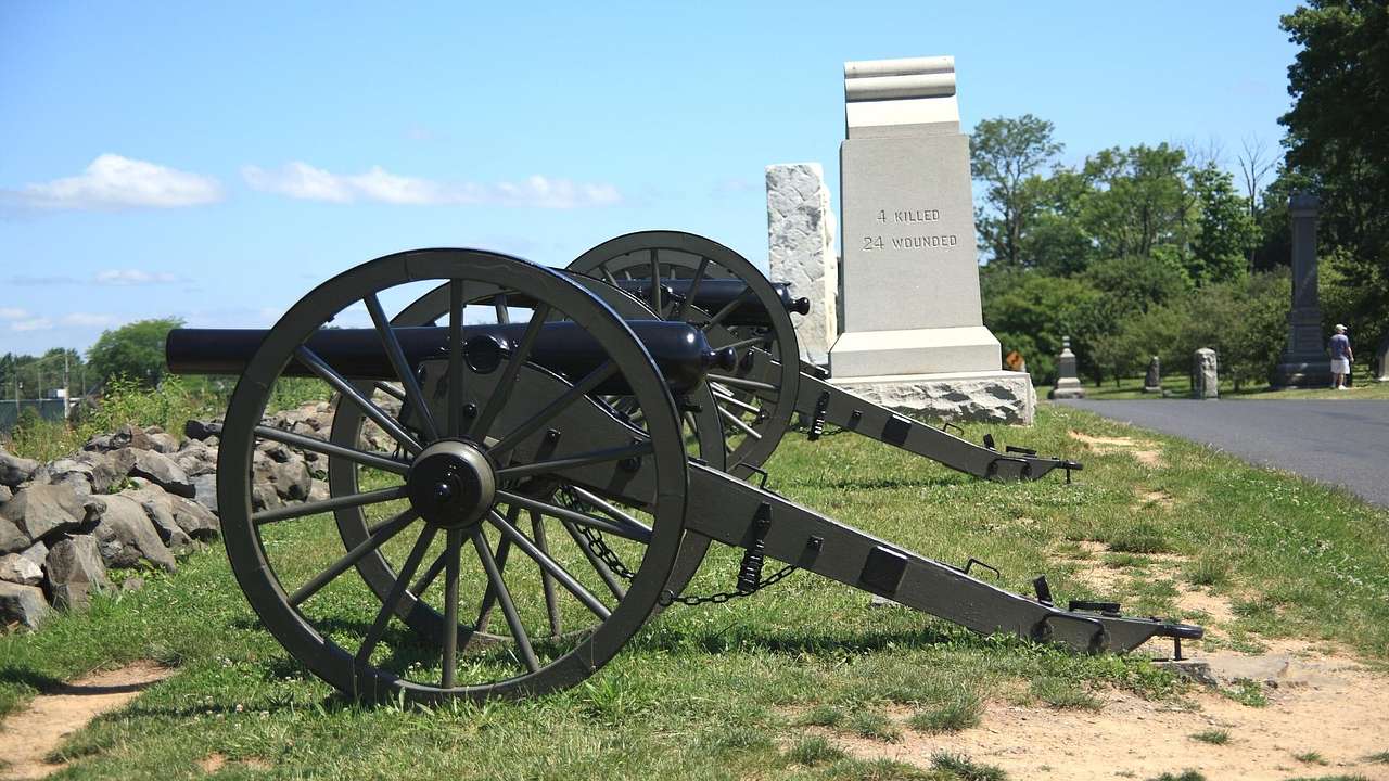Two cannons on the grass next to a stone monument on a clear day
