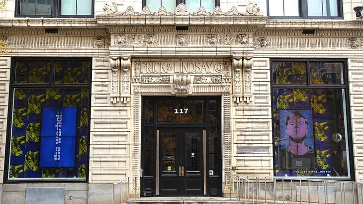 A stone building entrance with Andy Warhol prints in the windows