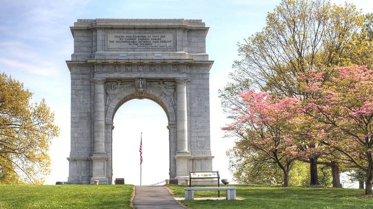 A stone arch in a park with autumn trees and blue sky around it