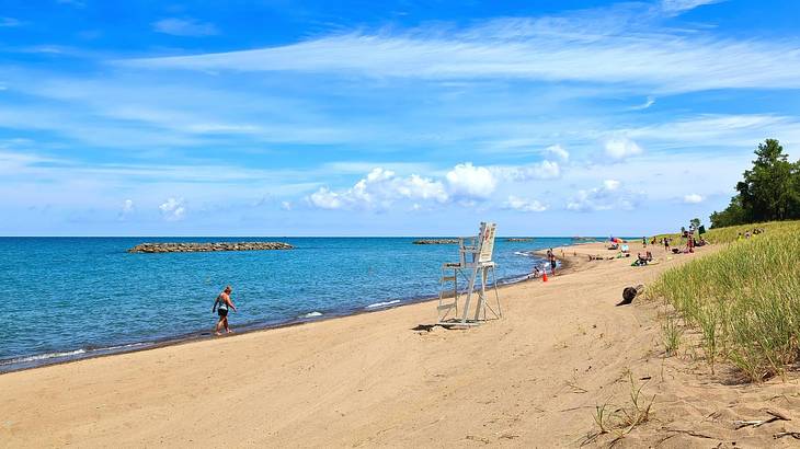 A sandy beach with a wooden lifeguard's chair and greenery next to the ocean