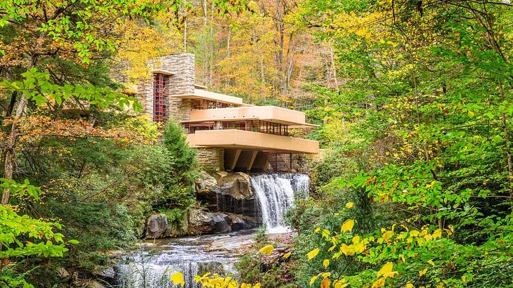 A modern home with a waterfall next to it and greenery surrounding it