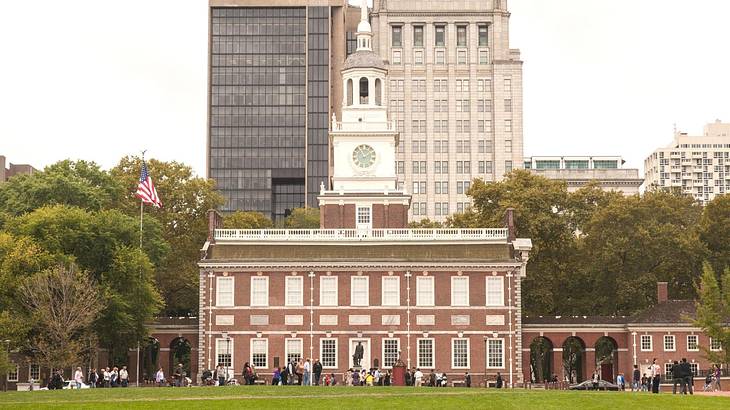 A redbrick building with a white tower and windows, next to grass, trees & buildings