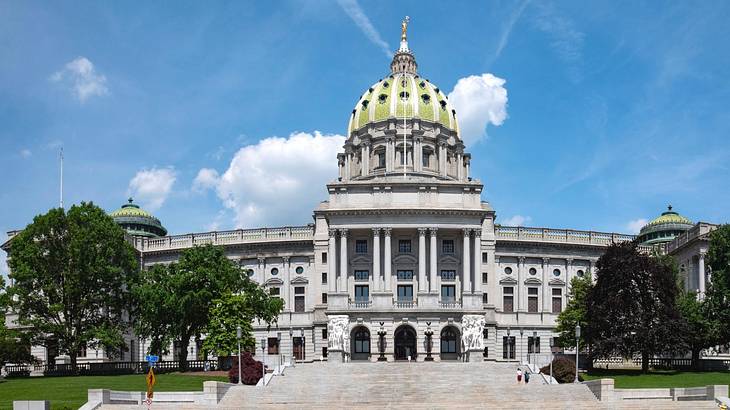 A grand state capitol building with columns and a domed roof and trees in front