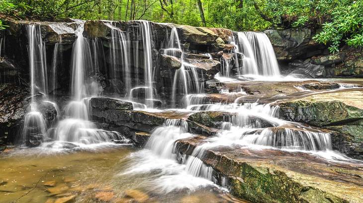 A waterfall with many streams of water flowing into a river surrounded by greenery