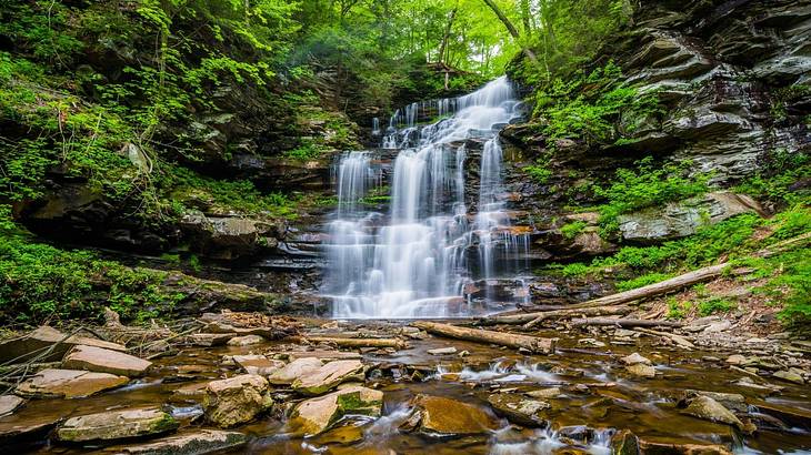 A waterfall flowing over rocks surrounded by greenery