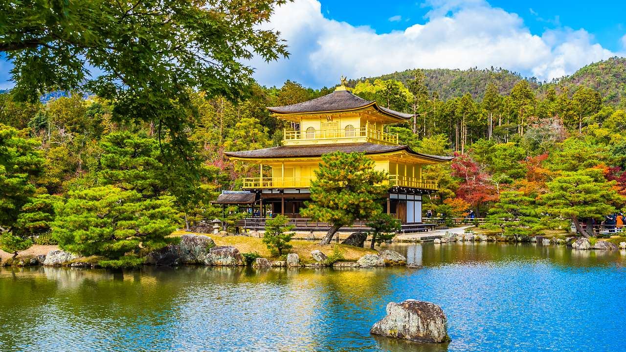 A yellow Japanese pavilion in the middle of a forest, overlooking a lake