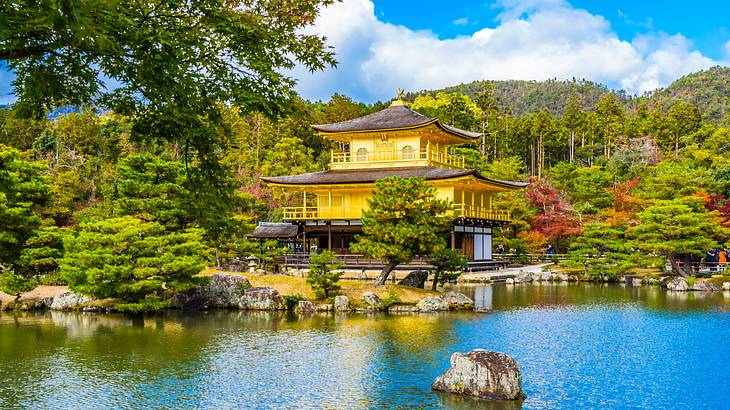 A yellow Japanese pavilion in the middle of a forest, overlooking a lake