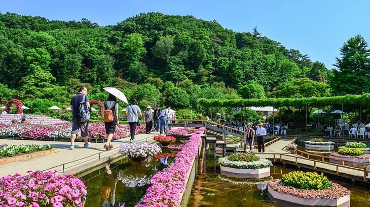 People walking around a colorful garden with small ponds and green trees at the back