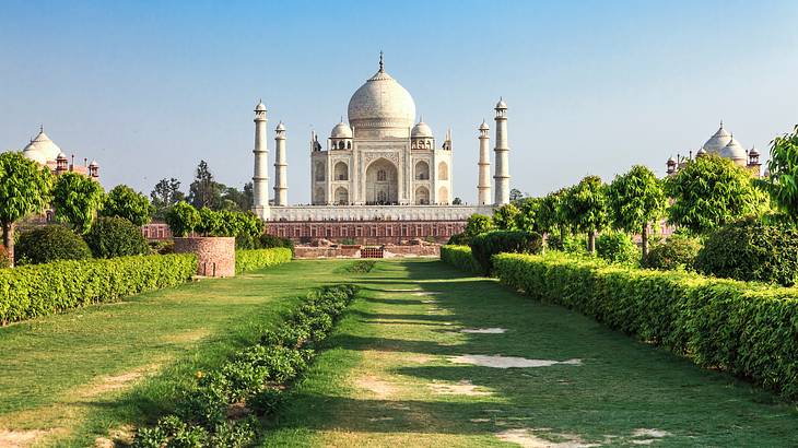 A magnificent white marble palace-like mausoleum facing a lawn lined with bushes