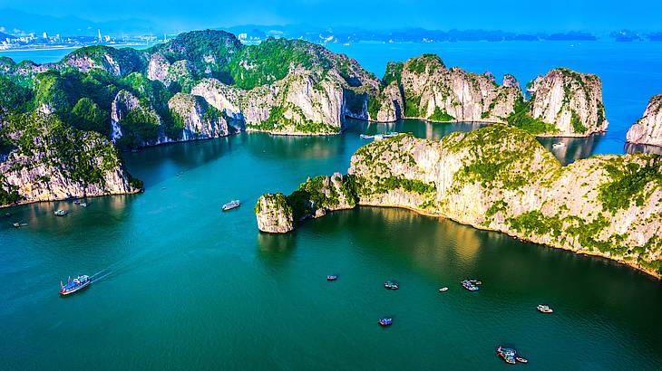 Many boats floating on calm water with green rocky cliffs all around