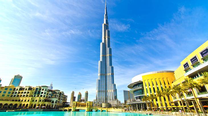 A skyscraper against a blue sky towering over buildings facing a body of water