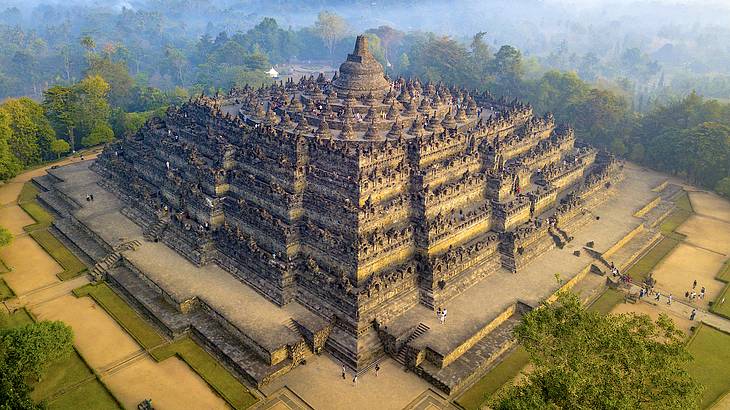 Top view of many pointy tops of a stone temple with a foggy background of greenery