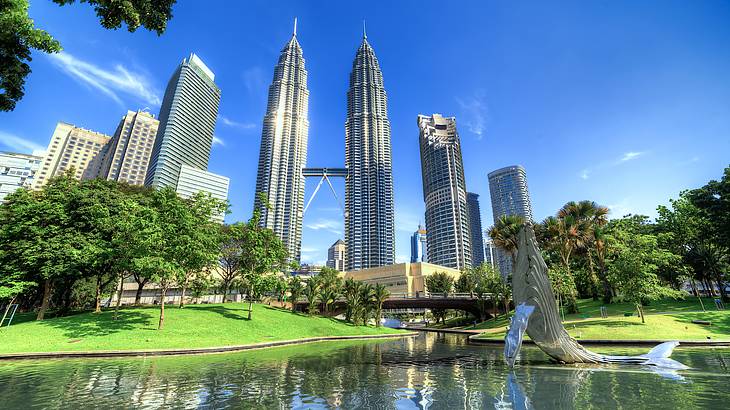 Two large steel-structured towers connected by a bridge from far away facing a pond