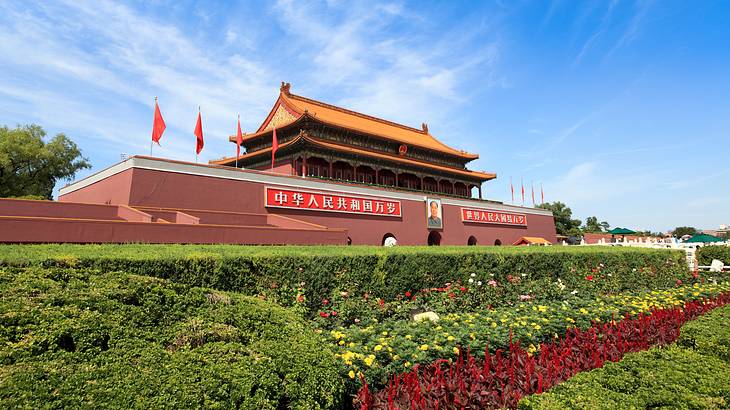 Green hedges in front of the entrance to a big Chinese temple with red flags