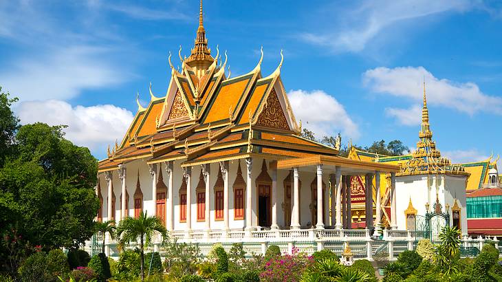 Two white temples with golden roofs and trees in front on a sunny day