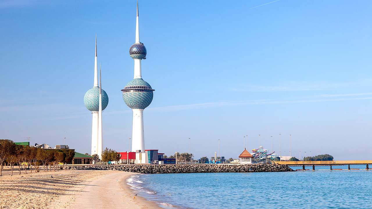 Three white towers with blue spheres along a sandy beach with blue water