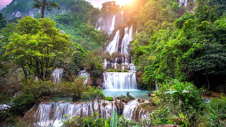 Many small waterfalls cascading down from the top of a forest into water below