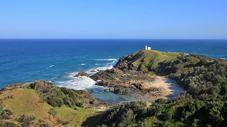 View of rocks, water and a small building on a green hill, Port Macquarie, NSW