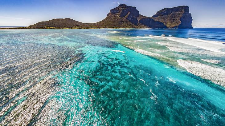 Sand, rocks, blue water, and peaks in the distance at Lord Howe Island, Australia