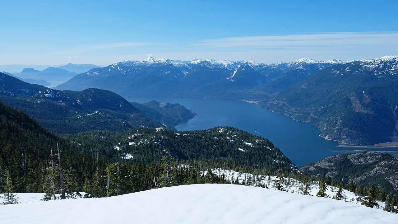 A snowy lookout point overlooking trees, mountains, and a body of water