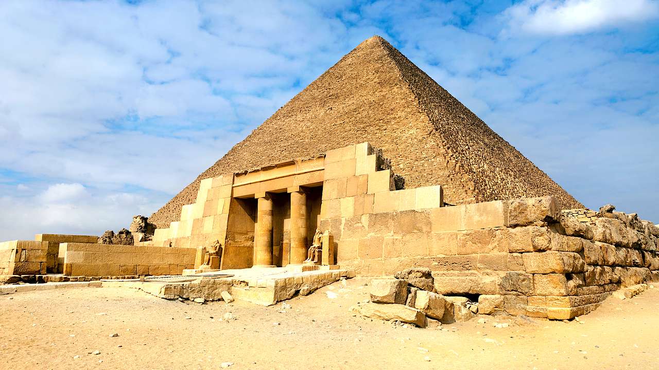 One of the Pyramids of Giza with an entrance of columns against a partly cloudy sky