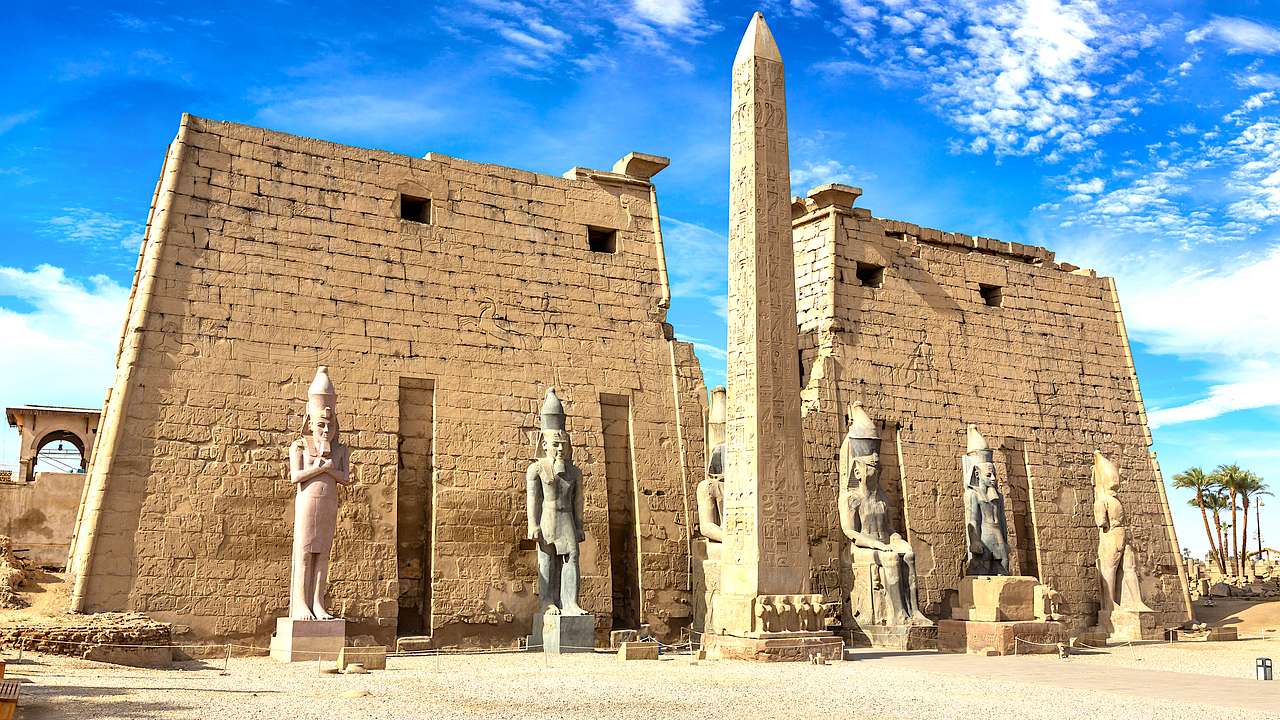 An entrance to an ancient Egyptian temple with statues and an obelisk in the center