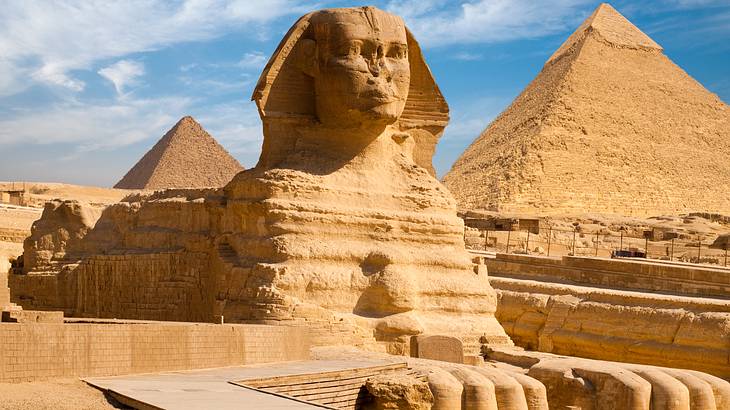 Statue of a sphinx with two large pyramids behind it situated in a desert