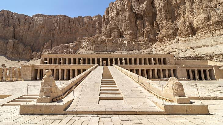 A stone pathway leading to an ancient Egyptian temple carved into the mountainside